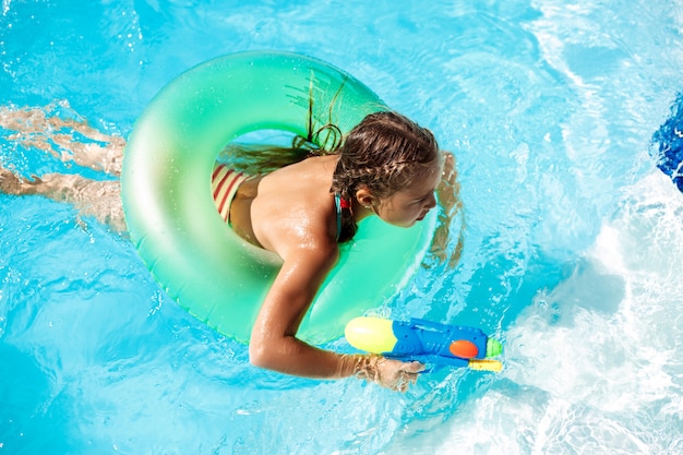 Bambini allegri che giocano a pistole ad acqua, gioendo, saltando, nuotando in piscina.