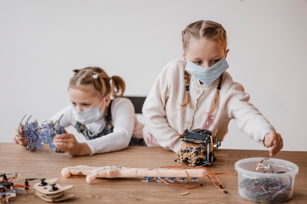 Bambini con maschere mediche che imparano a usare i componenti elettrici