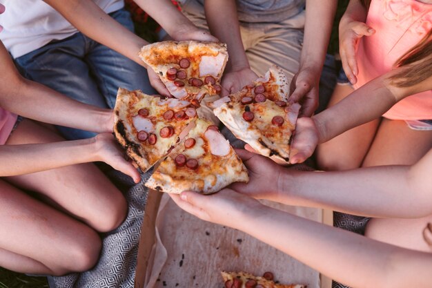 Bambini dell'angolo alto che prendono una fetta di pizza