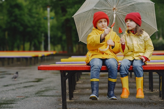 Bambini divertenti in stivali da pioggia che giocano in un parco piovoso