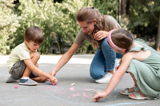 Bambini e insegnante del colpo pieno che disegnano sulla terra