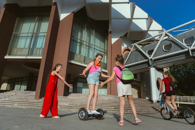 Bambini felici che giocano in strada della città nella soleggiata giornata estiva di fronte a un edificio moderno. Gruppo di bambini felici o adolescenti che hanno divertimento insieme