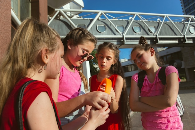 Bambini felici che giocano in strada della città nella soleggiata giornata estiva di fronte a un edificio moderno. Gruppo di bambini o adolescenti felici divertendosi insieme. Concetto di amicizia, infanzia, estate, vacanze.