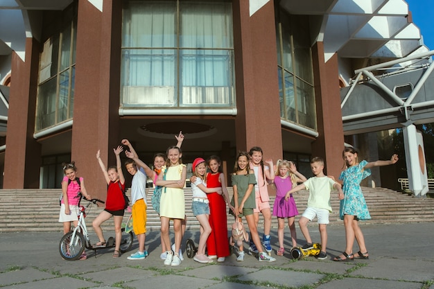 Bambini felici che giocano in strada della città nella soleggiata giornata estiva di fronte a un edificio moderno. Gruppo di bambini o adolescenti felici divertendosi insieme. Concetto di amicizia, infanzia, estate, vacanze.