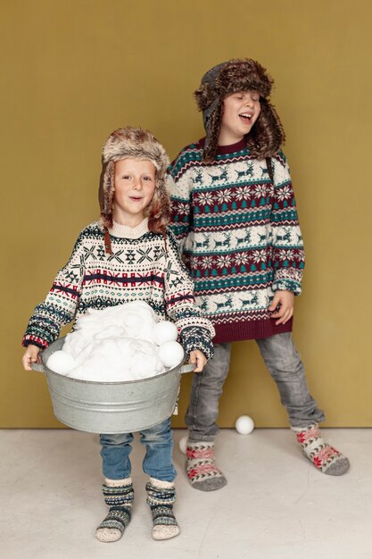 Bambini felici della foto a figura intera che giocano con le palle di neve all'interno