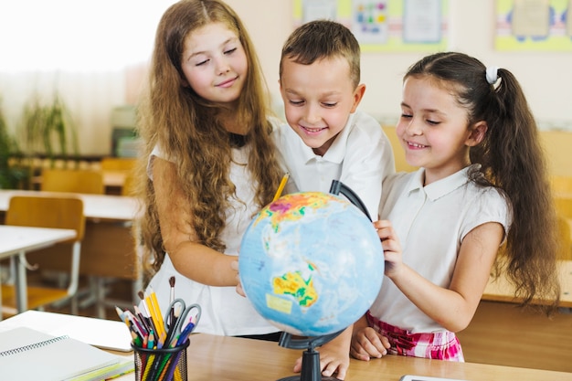 Bambini in piedi intorno al globo messo sul tavolo