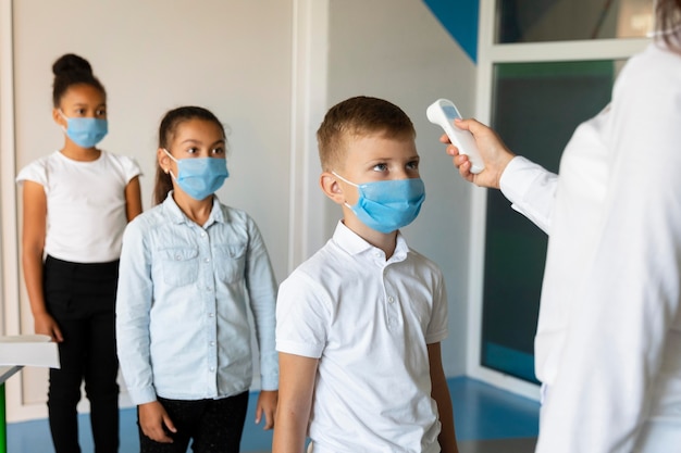 Bambini piccoli che aspettano in fila un insegnante per misurare la temperatura