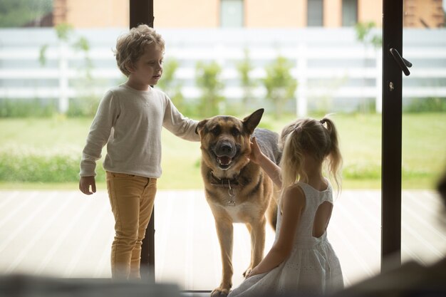 Bambini ragazzo e ragazza che giocano con il cane che entra all&#39;interno della casa