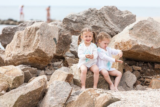 Bambini sulla spiaggia del mare. Gemelli seduti contro pietre e acqua di mare.