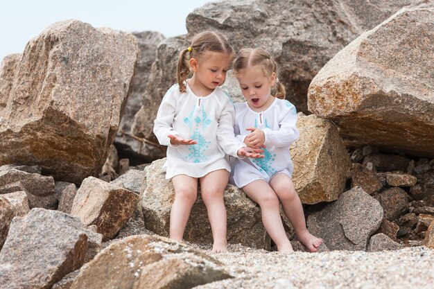 Bambini sulla spiaggia del mare. Gemelli seduti contro pietre e acqua di mare.