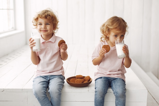 Bambini svegli che mangiano i biscotti e che bevono latte