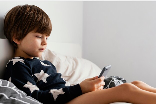 Bambino a letto tenendo lo smartphone