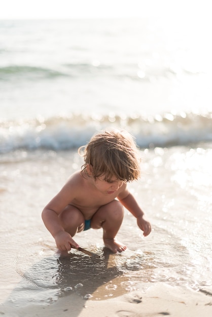 Bambino accovacciato che gioca in spiaggia