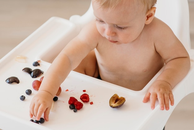 Bambino ad alto angolo nel seggiolone scegliendo quale frutta mangiare