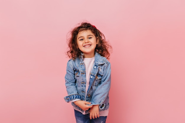 Bambino allegro del preteen con capelli ricci che ride della macchina fotografica. Studio shot di spensierata bambina isolata su sfondo rosa.