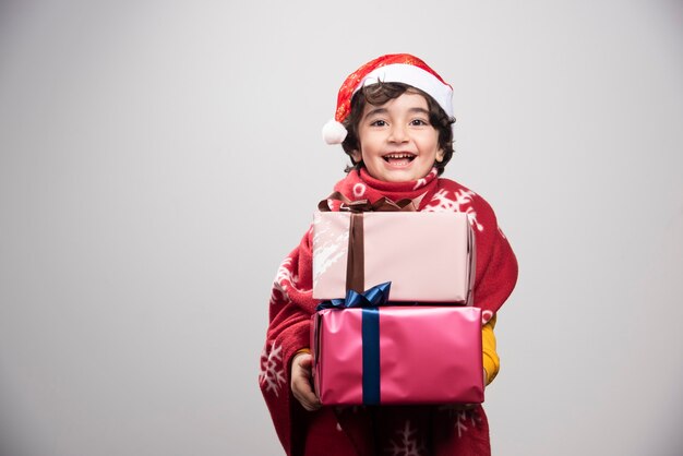 Bambino allegro in cappello di Babbo Natale che tiene i regali di Natale
