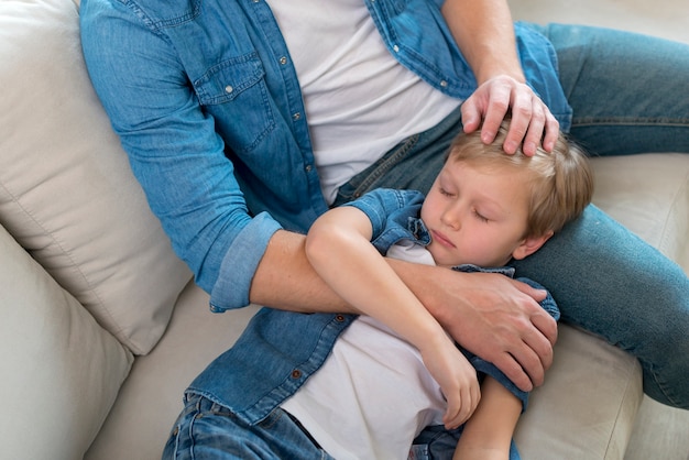 Bambino assonnato che riposa la testa sulle gambe del padre