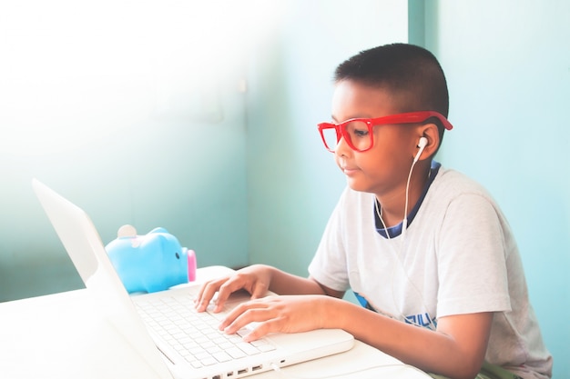 Bambino bambino che indossa occhiali rossi che ascolta e usando il computer portatile