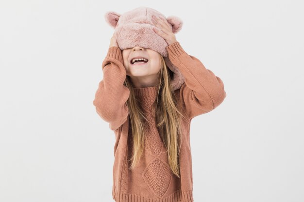 Bambino biondo che copre il viso con cappello invernale