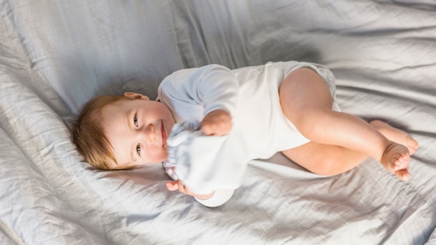 Bambino biondo sveglio di vista superiore in letto bianco