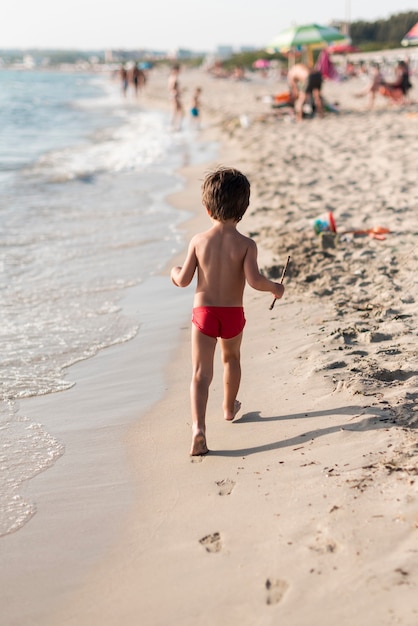 Bambino che cammina lungo la spiaggia da dietro