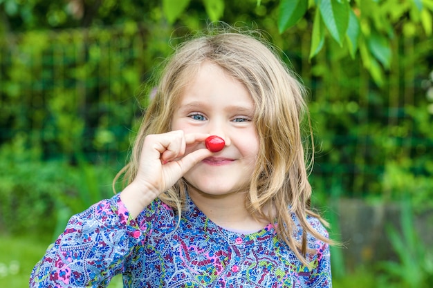 Bambino con la ciliegia in mano in un giardino