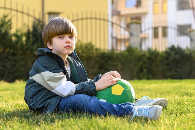 Bambino della foto a figura intera che si siede sull'erba