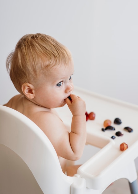 Bambino di lato nel seggiolone scegliendo quale frutta mangiare