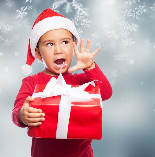 Bambino divertente in possesso di un regalo di Natale con la mano destra