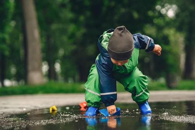 Bambino divertente in stivali da pioggia che giocano in un parco di pioggia