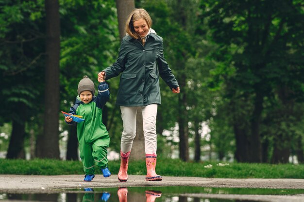 Bambino divertente in stivali da pioggia che giocano in un parco di pioggia