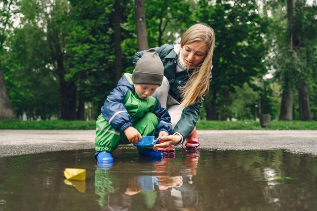 Bambino divertente in stivali da pioggia che giocano in un parco di pioggia