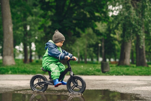 Bambino divertente in stivali da pioggia che giocano in un parco di pioggia