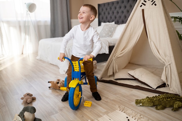 Bambino felice a tutto campo con triciclo al chiuso