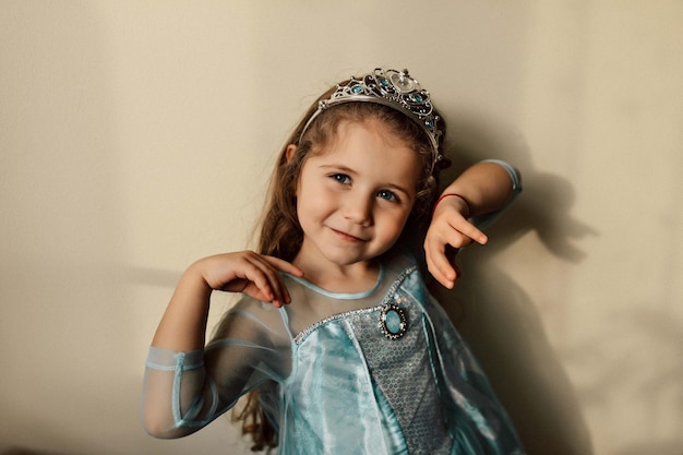 Bambino felice con lunghi capelli ondulati in posa davanti alla telecamera con felici vere emozioni Ritratto in studio di una bambina di compleanno indossa un grazioso abito da festa e una corona