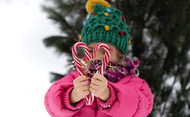 Bambino felice con un grande bastoncini di zucchero sotto un albero di Natale. Concetto di vacanze invernali.