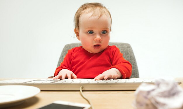 Bambino felice della neonata del bambino che si siede con la tastiera del computer isolata su un fondo bianco
