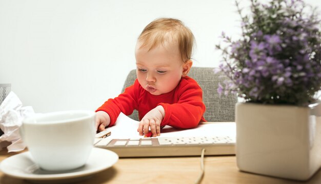Bambino felice della neonata del bambino che si siede con la tastiera del computer isolata