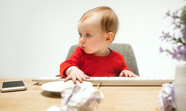 Bambino felice della neonata del bambino che si siede con la tastiera del computer su un bianco