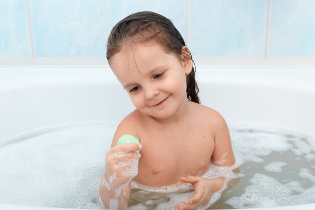 Bambino felice fare il bagno da solo, giocando con le bolle di schiuma e il suo nuovo giocattolo.