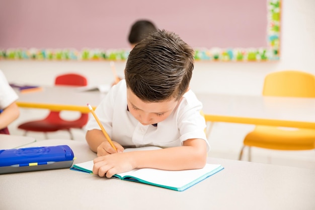 Bambino in età prescolare maschio che indossa l'uniforme e lavora su un compito di scrittura in classe