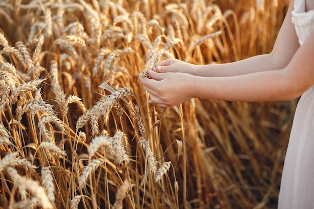 Bambino in un campo di grano estivo. Bambina in un vestito bianco carino.