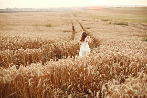 Bambino in un campo di grano estivo. Bambina in un vestito bianco carino.