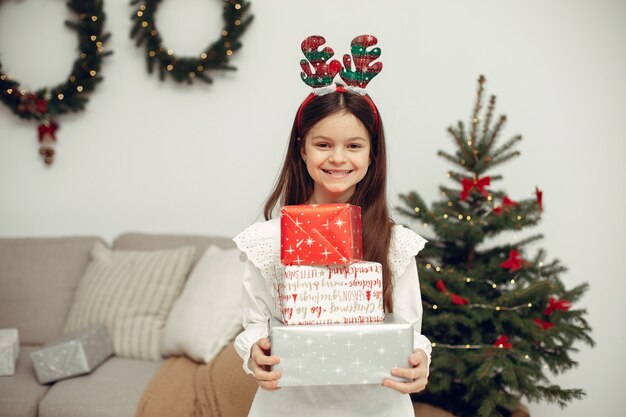 Bambino in un maglione bianco. Figlia che si siede vicino all'albero di Natale.