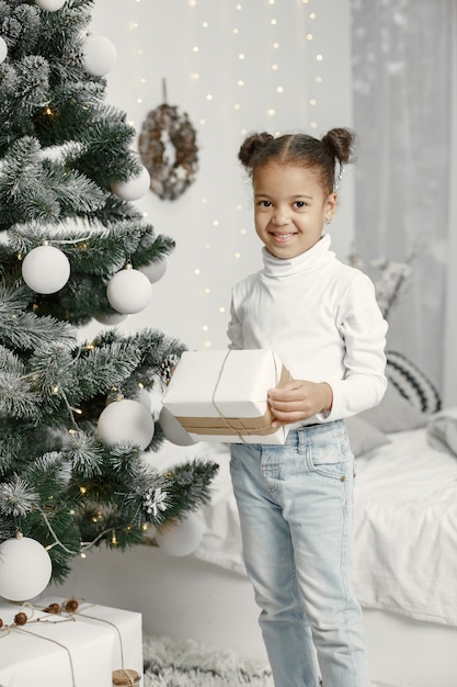 Bambino in un maglione bianco. Figlia in piedi vicino all'albero di Natale.