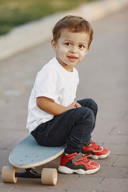 Bambino in un parco estivo. Ragazzo in una maglietta bianca. Capretto con il pattino.