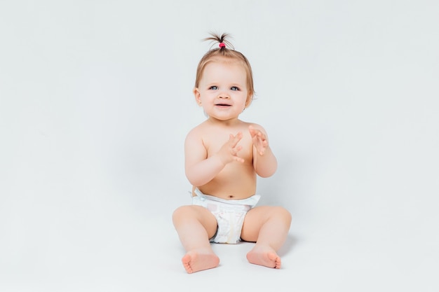 Bambino infantile della neonata che striscia felice guardando dritto isolato su un muro bianco