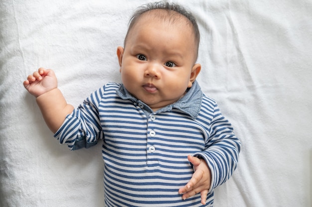 Bambino sdraiato a faccia in su su un letto bianco