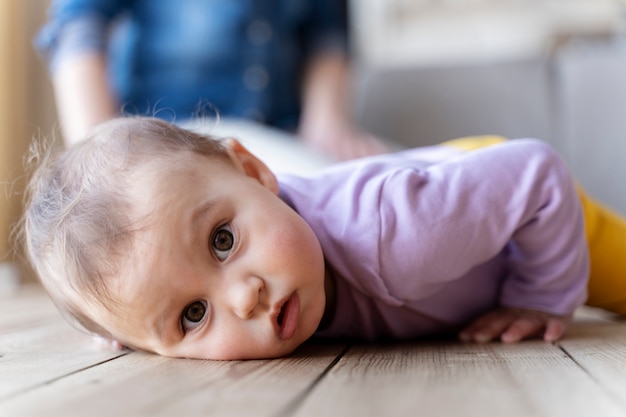 Bambino sdraiato sul pavimento mentre la madre sfocata è nella sua schiena