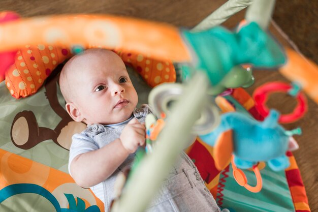 Bambino sdraiato sul tappeto in via di sviluppo guardando giocattoli appesi